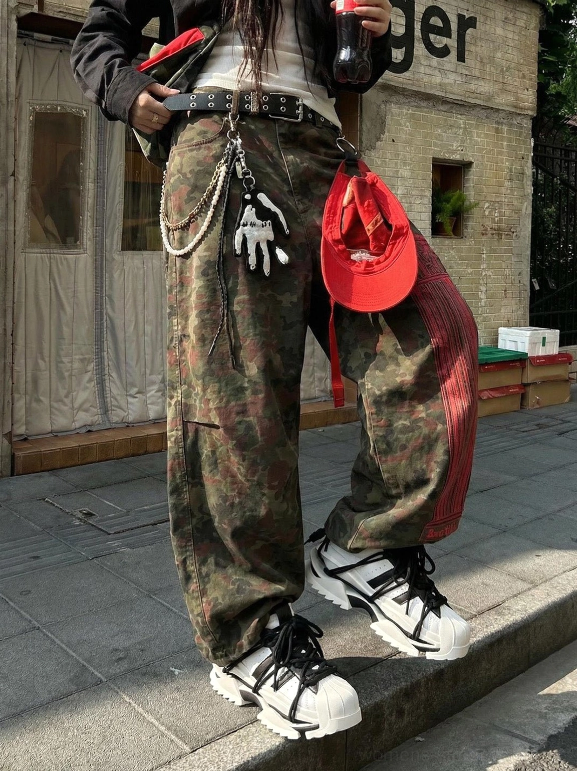 Black and white sculpted sole sneakers styled with camo cargo pants and a red waist bag in a contemporary punk streetwear outfit
