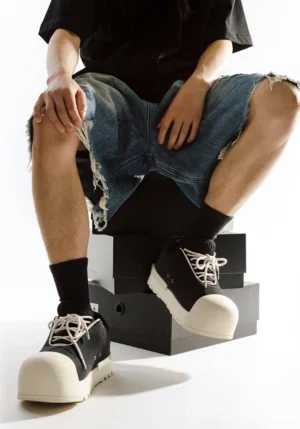 Model wearing black and white sculpted toe chunky platform low boots with black socks and frayed denim shorts