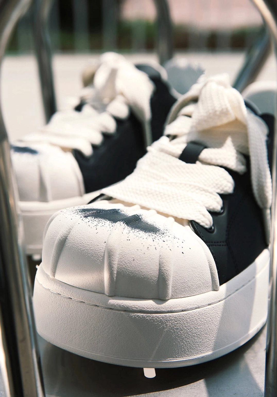 Front close-up of black and white shell toe skate-inspired platform derby sneakers with oversized white laces, spray-effect toe caps, and durable rubber soles