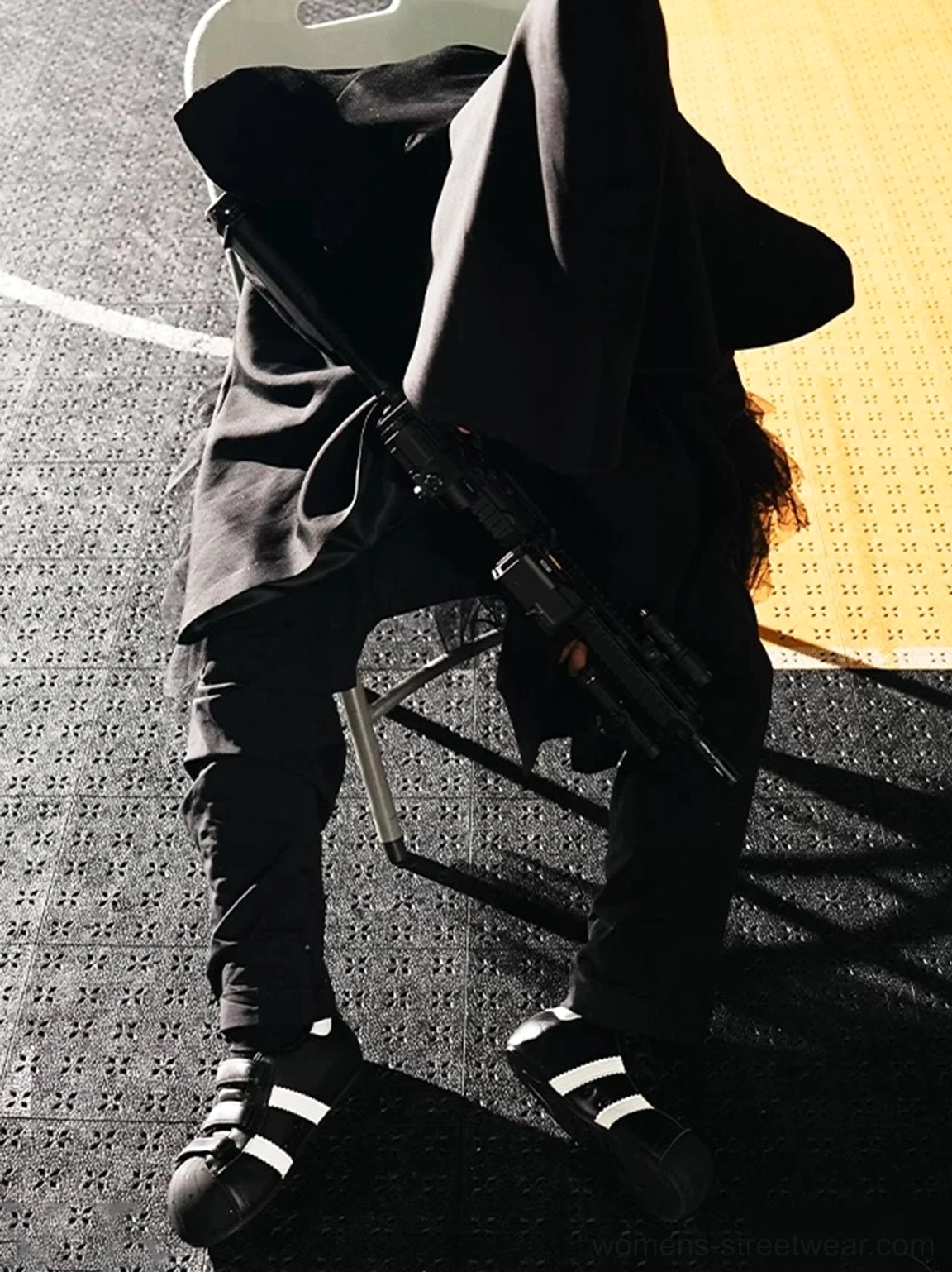 Black and white shell toe strap sneakers worn with an all-black streetwear outfit in a studio setting