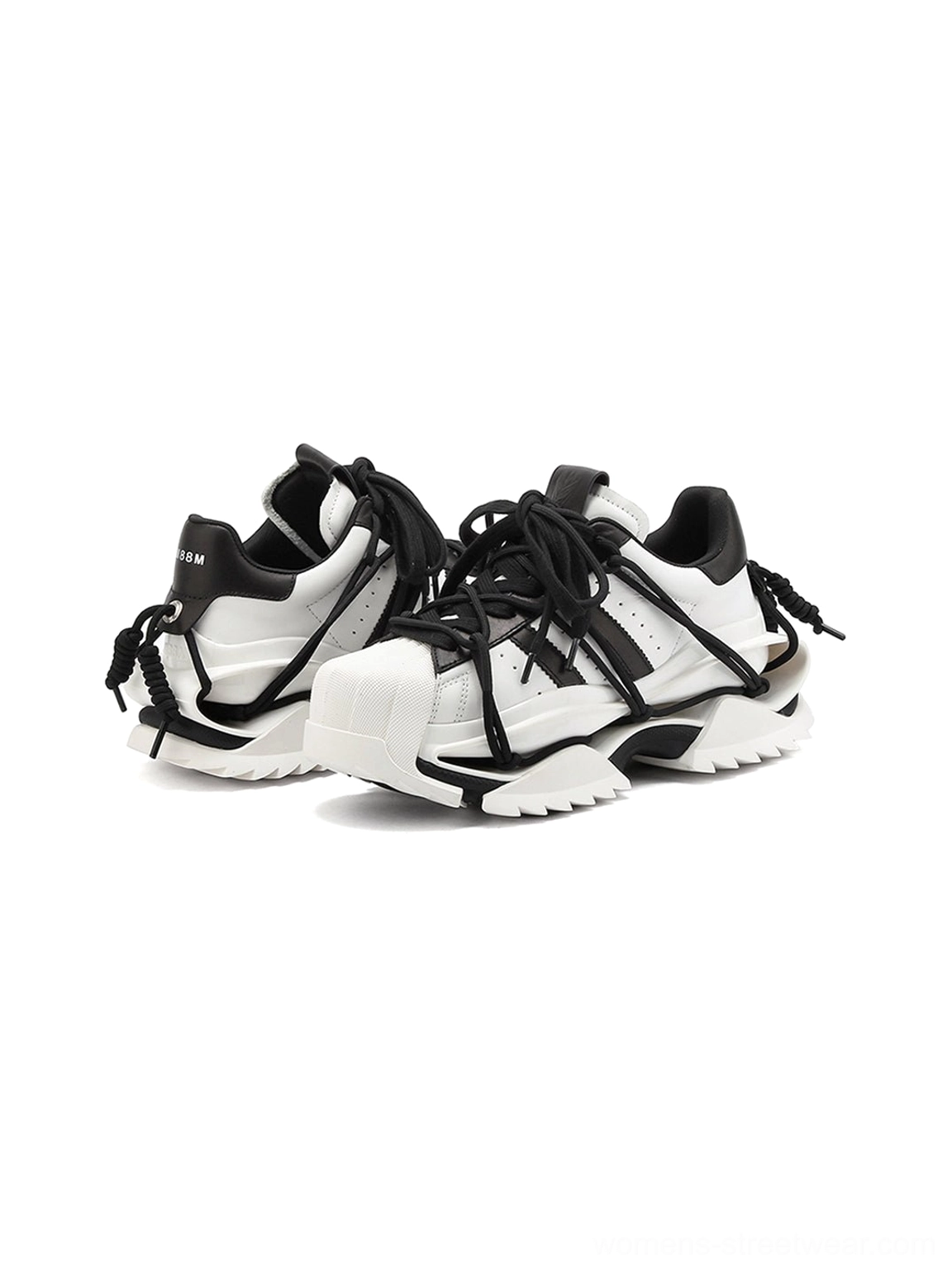 Rear studio view of black and white strapped sneakers showing pull tabs, decorative rear cords, contrast panels, and segmented chunky outsole