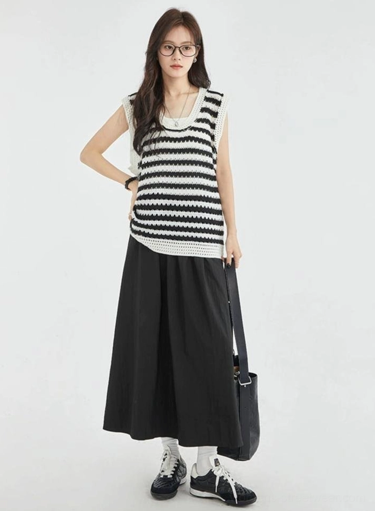Full front view of a black and white striped crochet sleeveless vest top styled with a black skirt, loafers, and shoulder bag for a Korean streetwear outfit