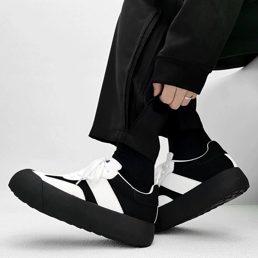 Black and white vintage chunky sneakers worn with black casual pants showing a thick platform sole layered upper and retro streetwear silhouette