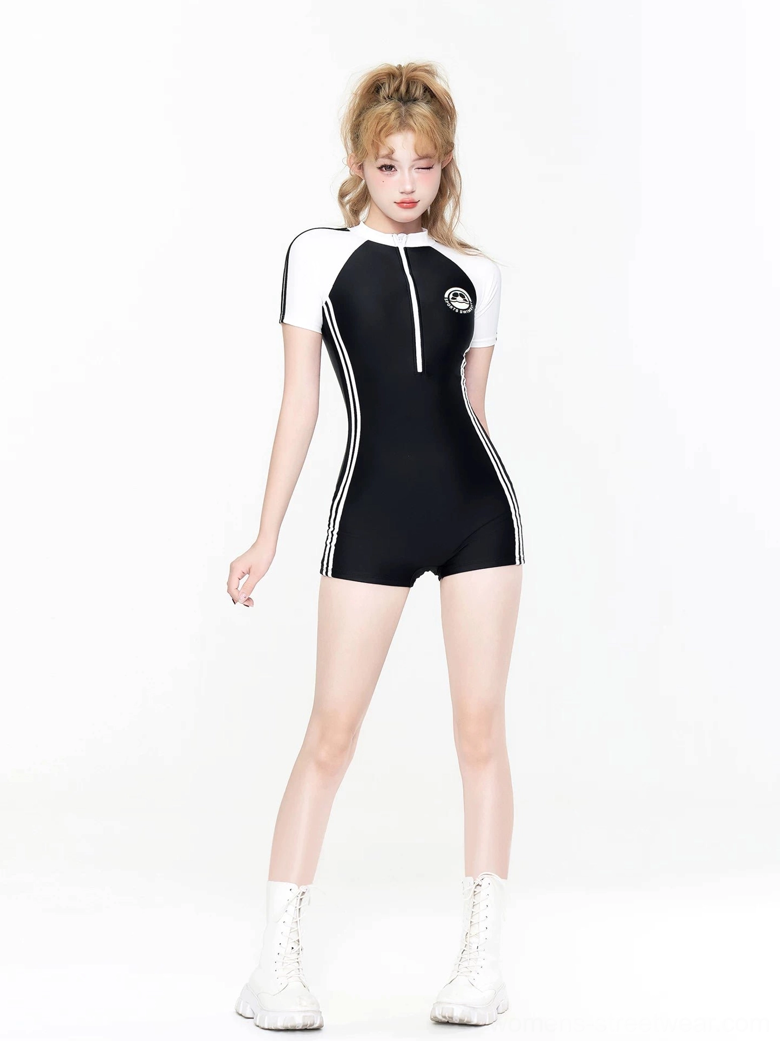 Front standing view of a black and white zip-front swim romper with varsity color blocking, short sleeves, chest patch, white side stripes, and athletic shorts