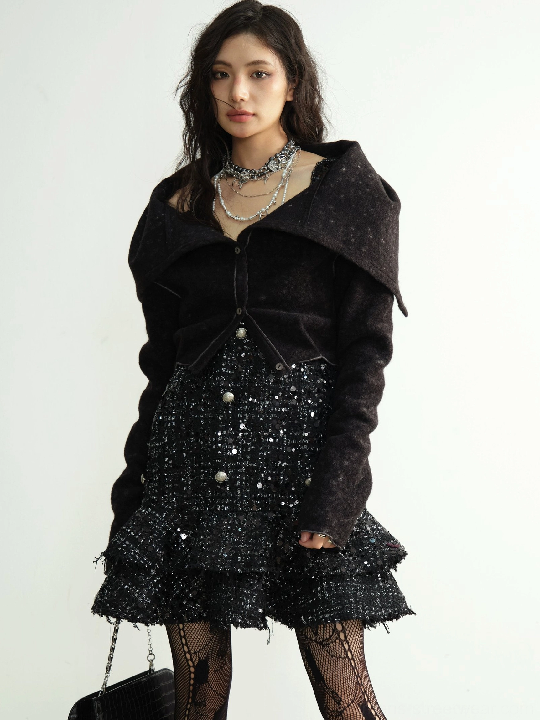 Front view of a black wide-collar cropped knit cardigan with pearl-style buttons, layered necklaces, and tiered ruffle tweed skirt