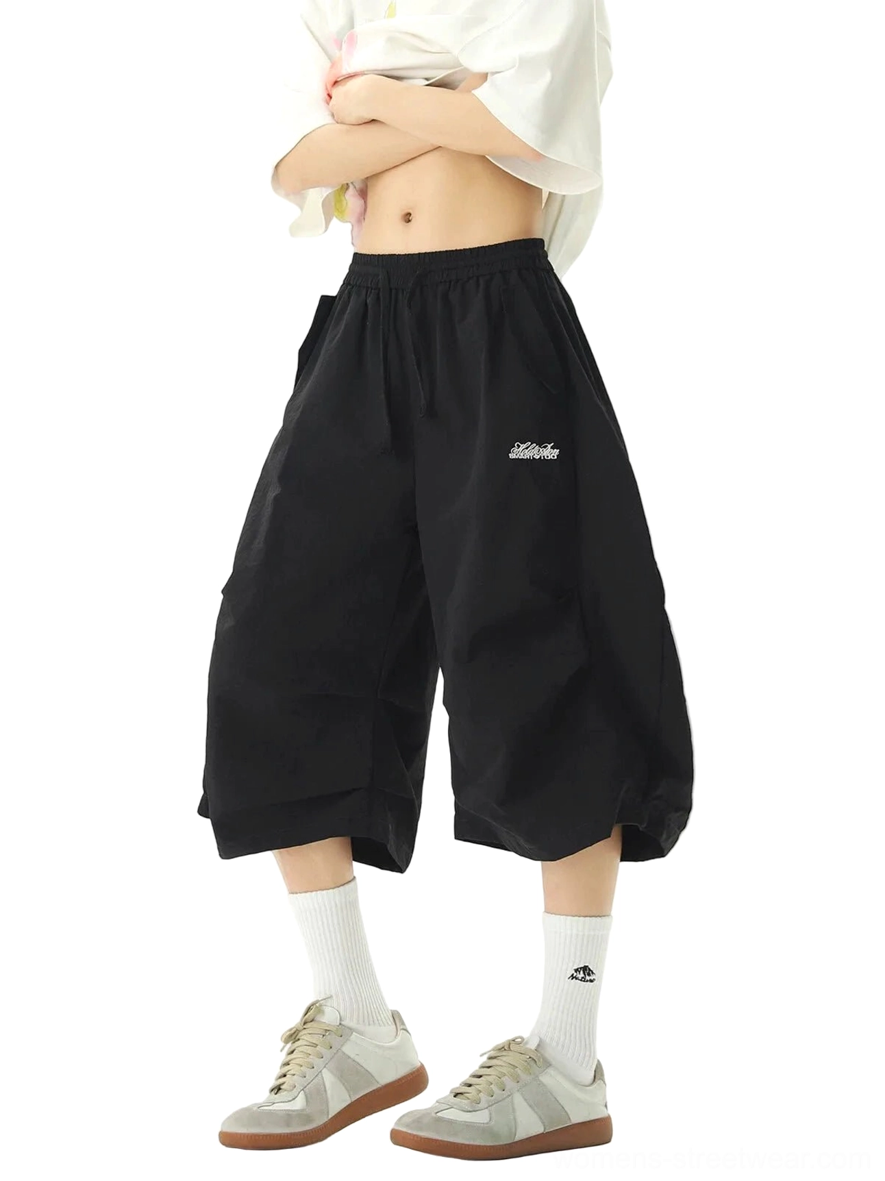 Black wide-leg balloon jogger shorts with three-dimensional pleats, elastic drawstring waistband, cropped length, and subtle embroidered logo styled with a white top