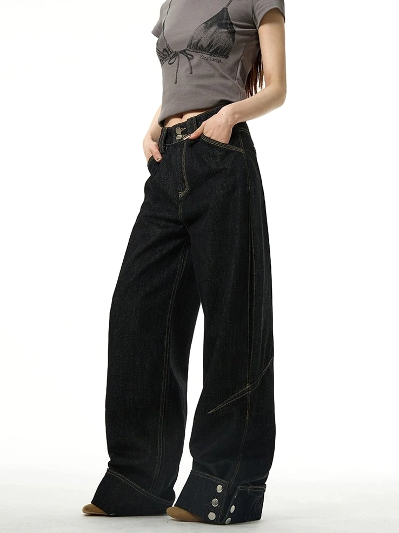 Three-quarter front view of black wide-leg cuffed jeans with buttoned hems and contrast stitching styled with a gray cropped graphic tee