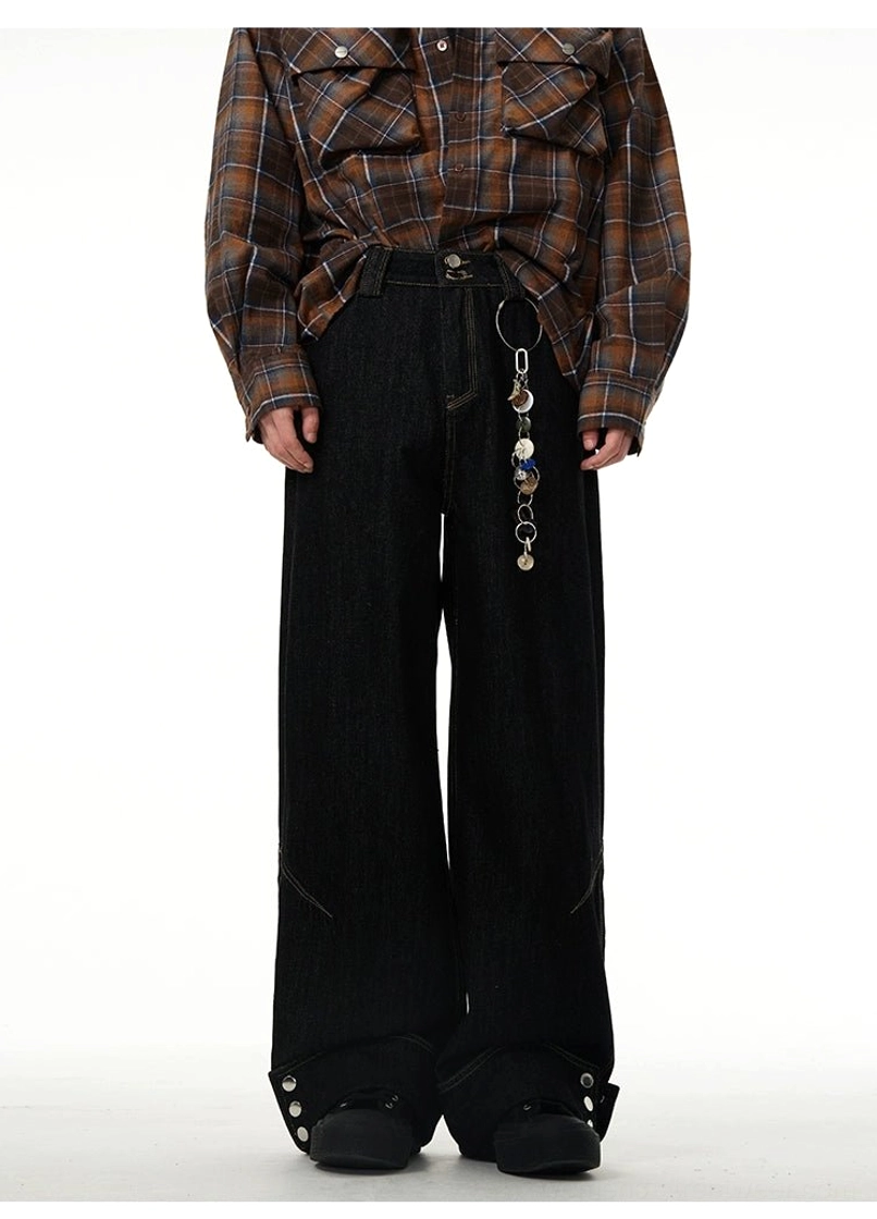 Front view of black wide-leg jeans with buttoned rolled cuffs styled with a plaid shirt and decorative metal chain