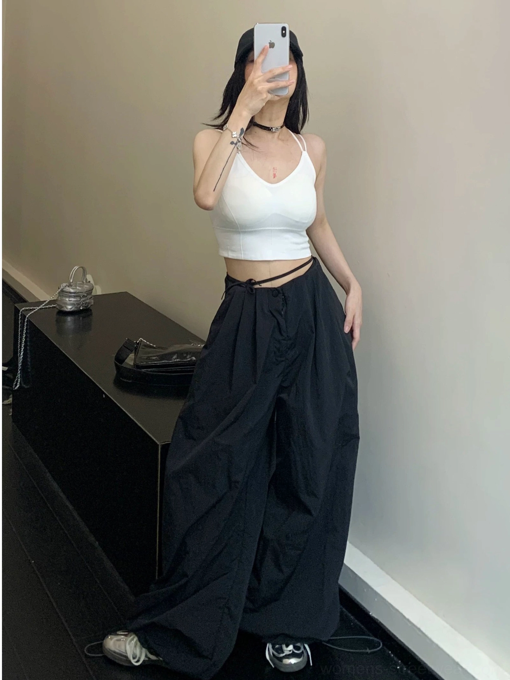 Black wide-leg parachute streetwear pants shown in a front mirror selfie with adjustable drawstring waist and relaxed pleats