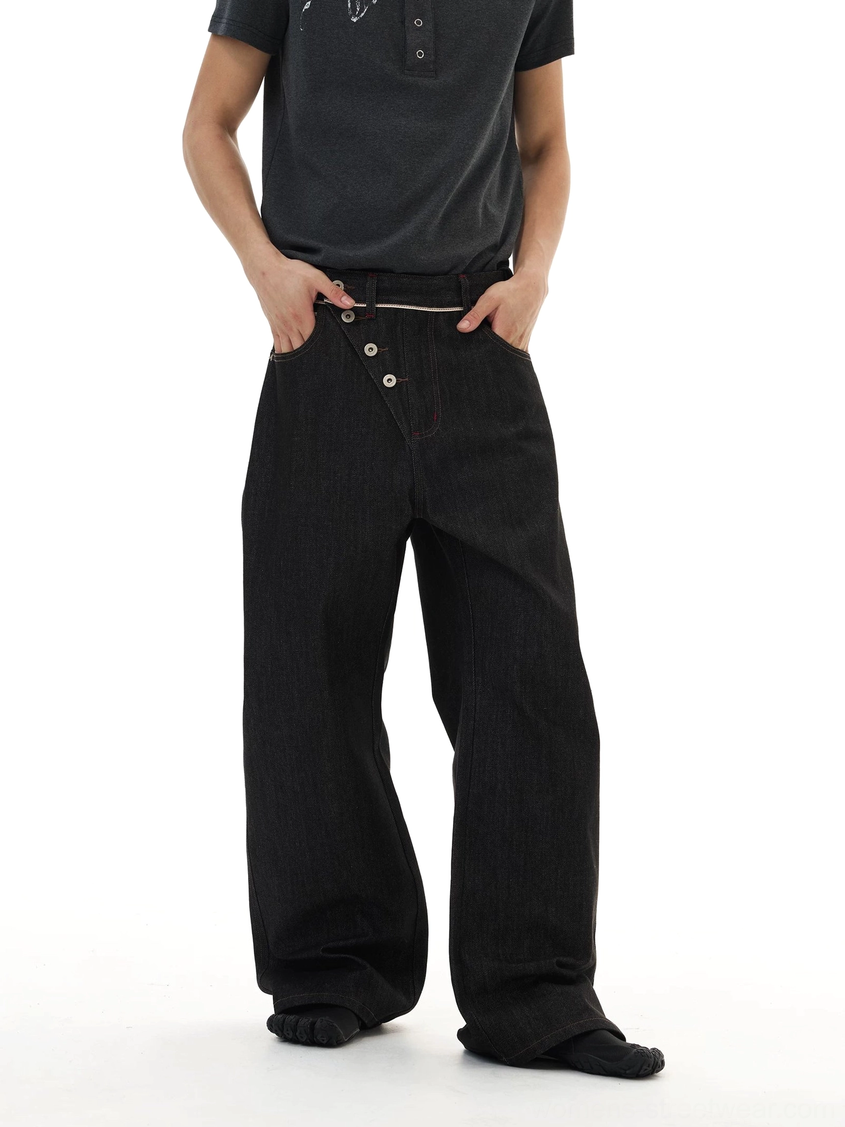 Front view of black wide-leg streetwear jeans with exposed asymmetric buttons and relaxed oversized fit on a male model