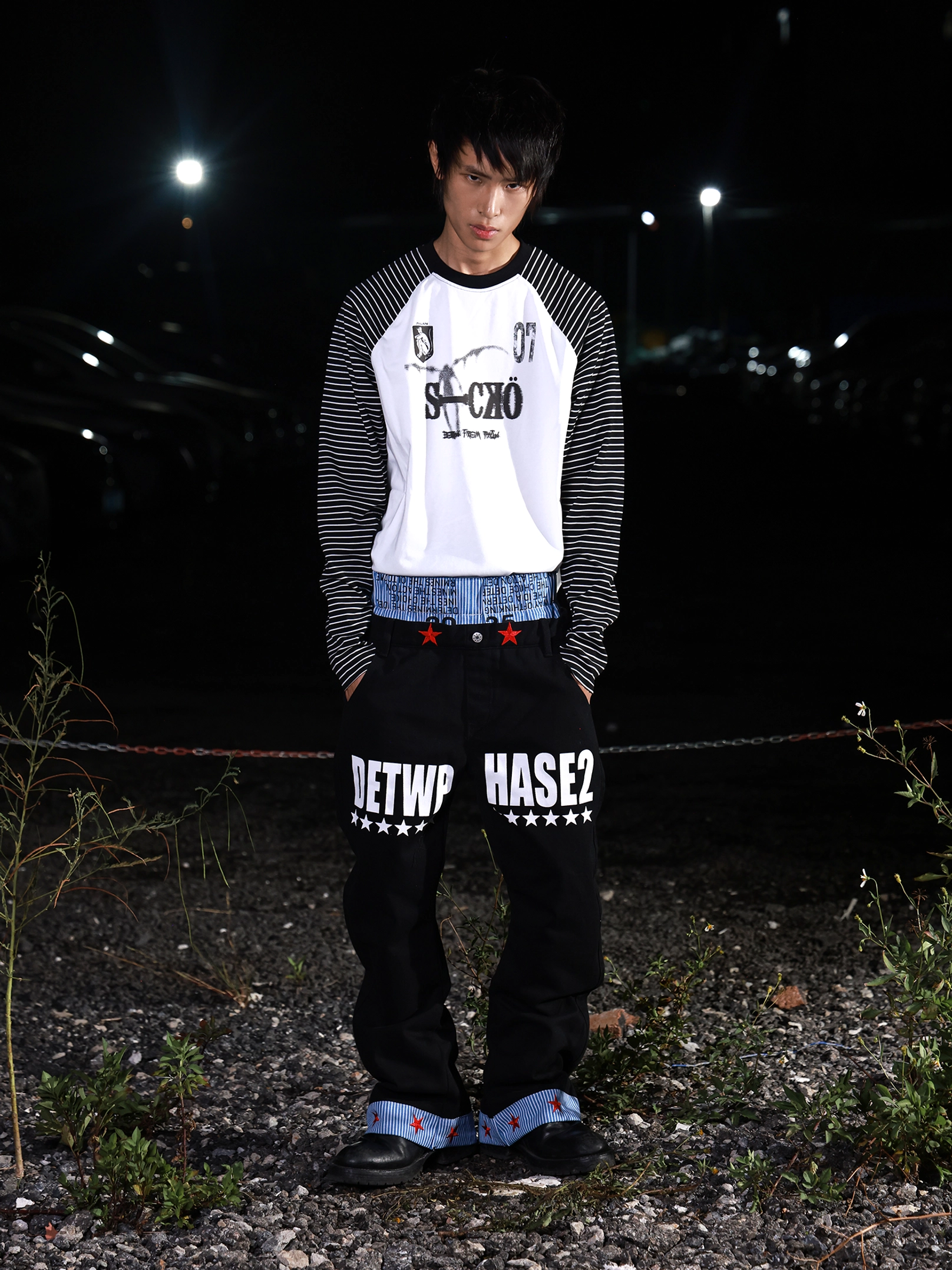Front view of black wide-leg streetwear jeans with white graphic lettering, star motifs, striped inner waistband, and red star turn-up cuffs