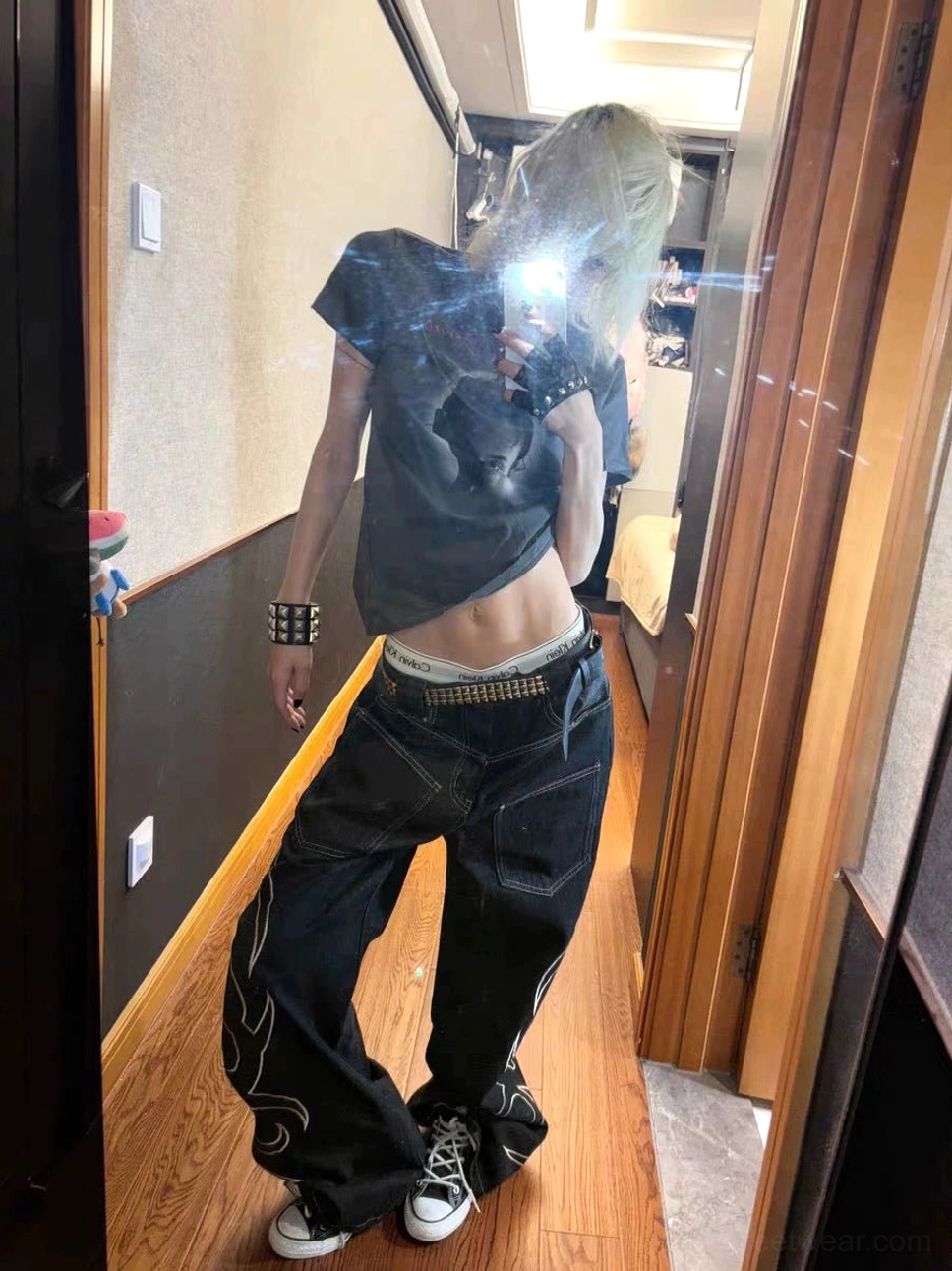 Mirror outfit view showing black wide leg streetwear jeans with swirling white tribal embroidery, relaxed fit, stacked hems, and casual sneakers