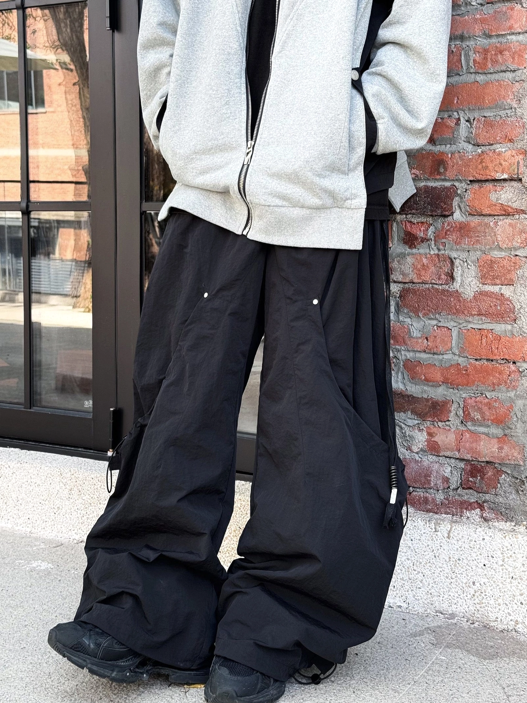 Black wide leg technical cargo pants styled with a grey zip up jacket and metal rivet seam details near a brick doorway