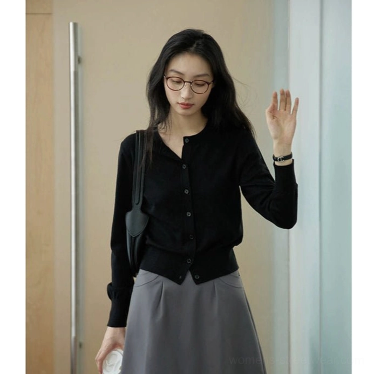 Black women's cropped crew neck button-up cardigan paired with a grey midi skirt and shoulder bag in a modern indoor foyer