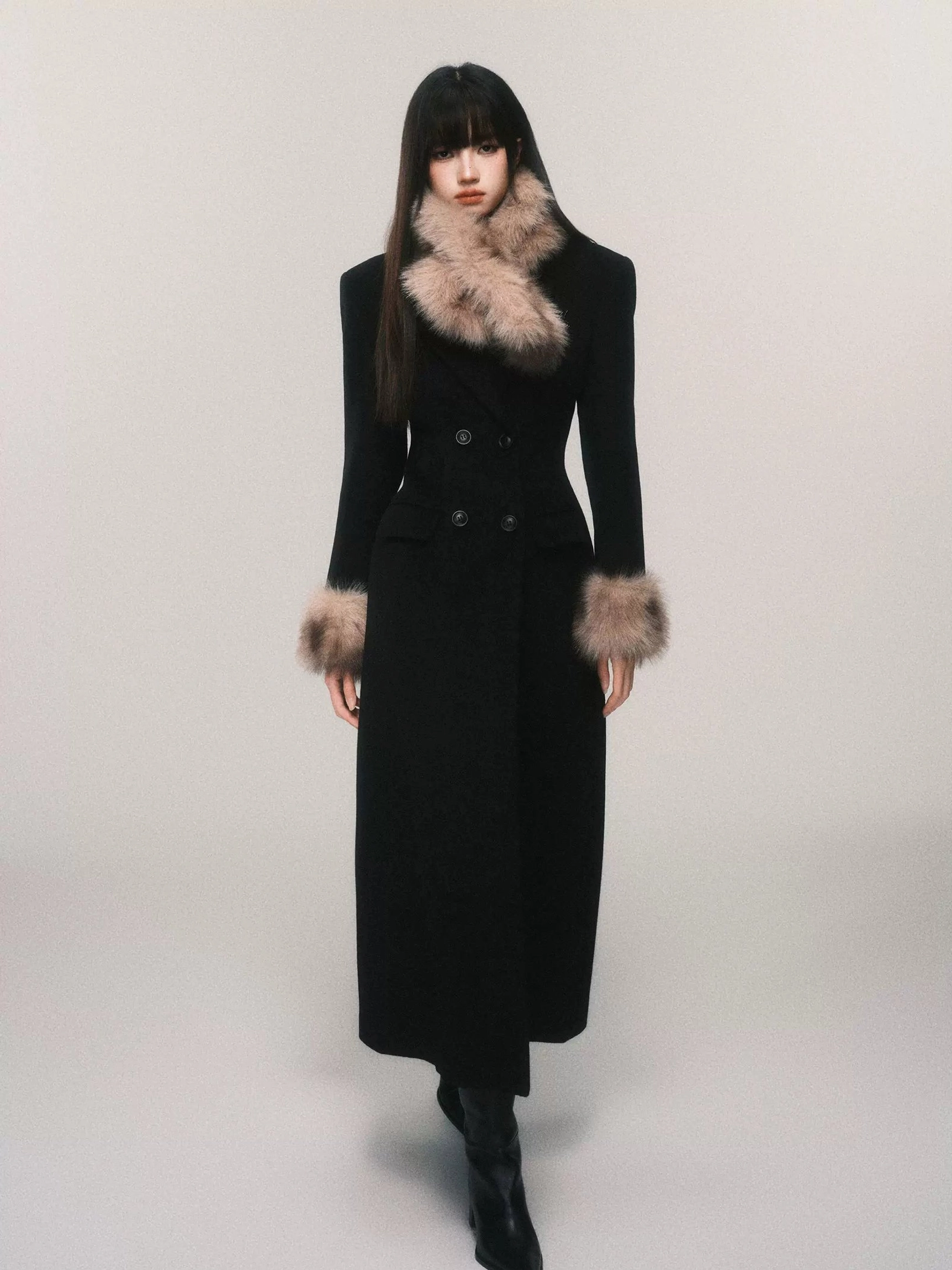 Black women's long tailored wool blend coat with faux fur cuffs shown while walking, featuring double-breasted buttons and maxi length