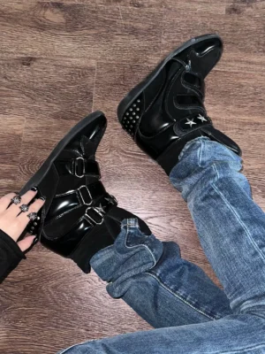 Black women’s hidden wedge high-top sneaker boots worn with blue jeans, featuring suede and patent-effect panels, triple hook-and-loop straps, star metal accents, and a studded heel