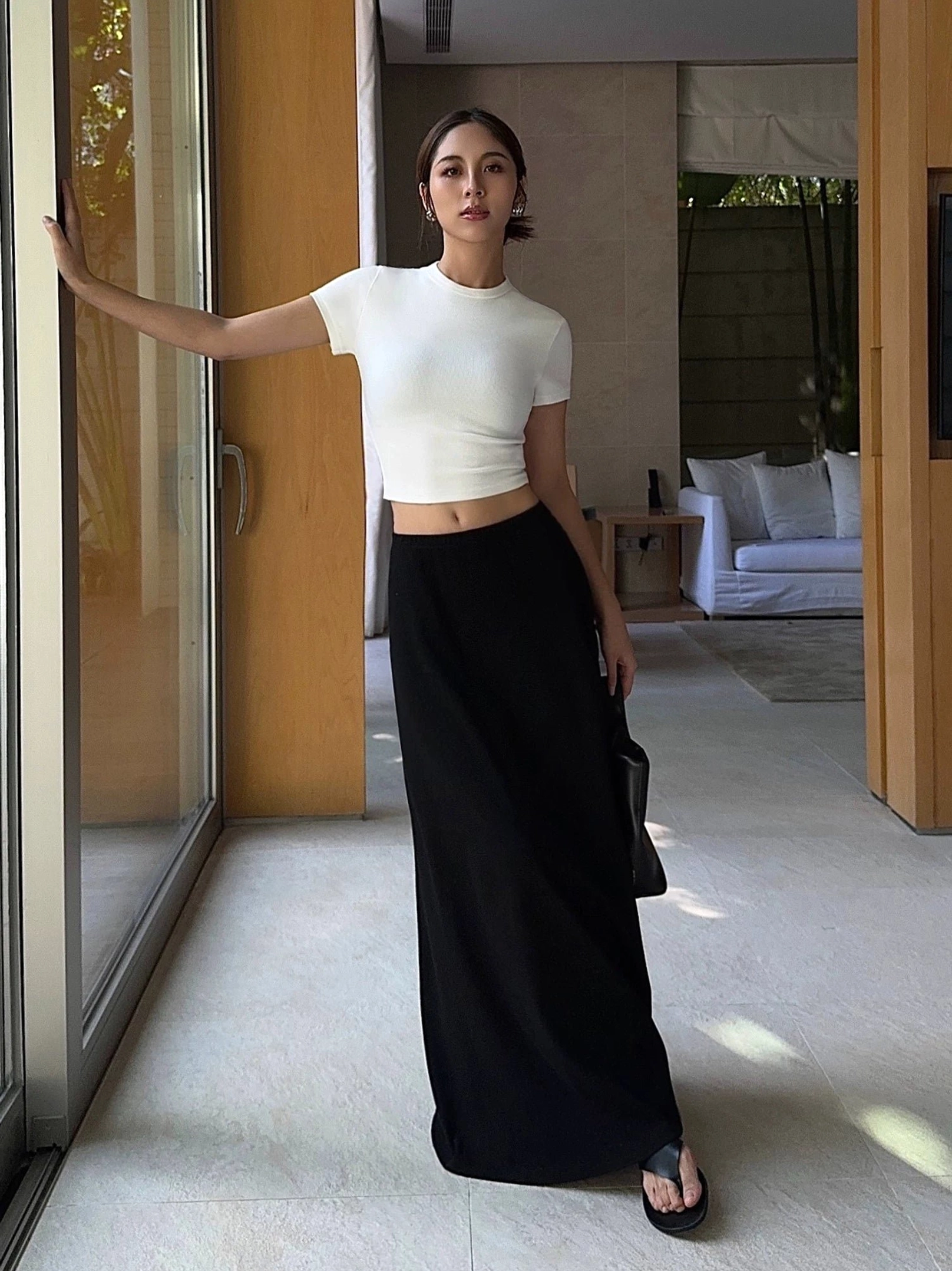 Black women's jersey maxi skirt with smooth full-length silhouette styled with a cropped white top and handbag