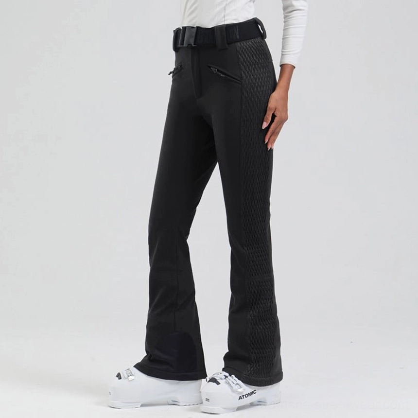 Low angle side view of black women's flared ski pants with quilted side panels, heel guards, zip pockets, and ski boots