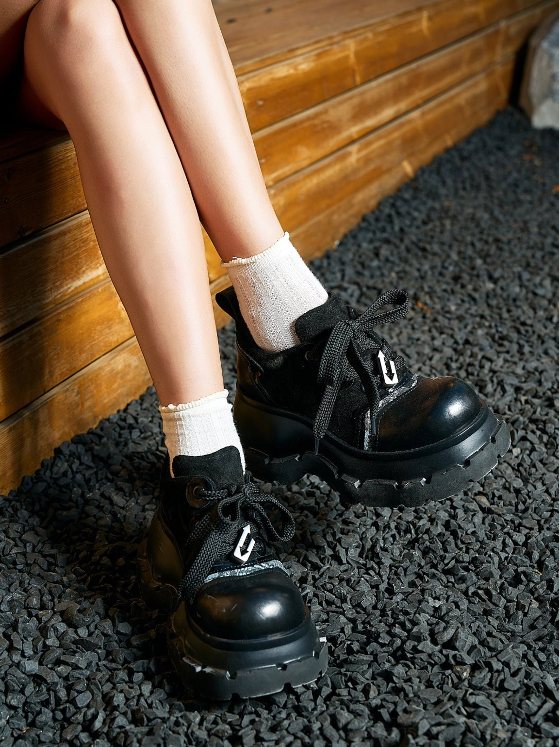 Side view of black women's streetwear derby shoes worn with white crew socks, thick platform sole, lace-up front, and rear heel pull tab
