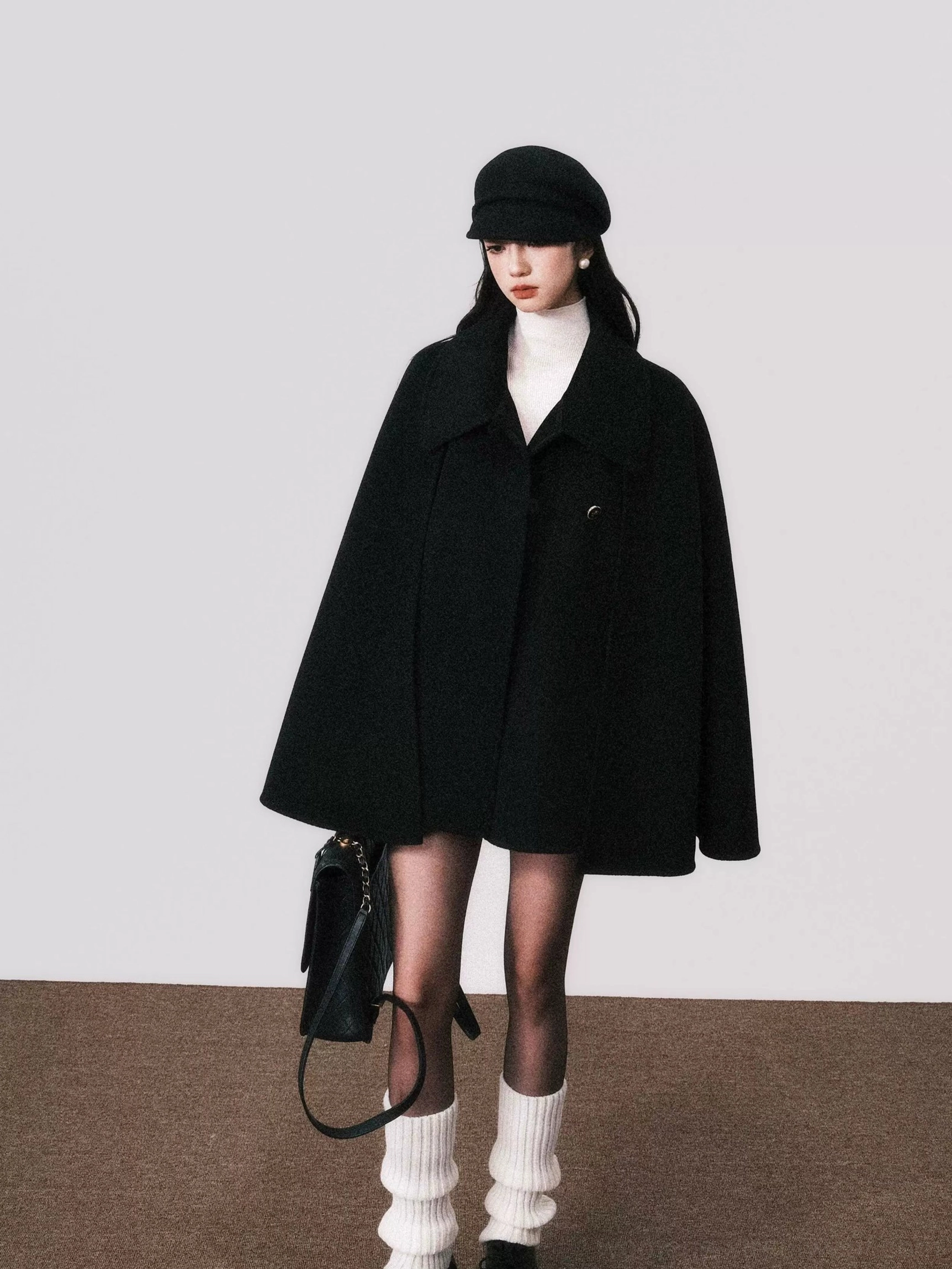 Model wearing an oversized black wool cape coat with a dramatic A-line silhouette in a studio fashion portrait