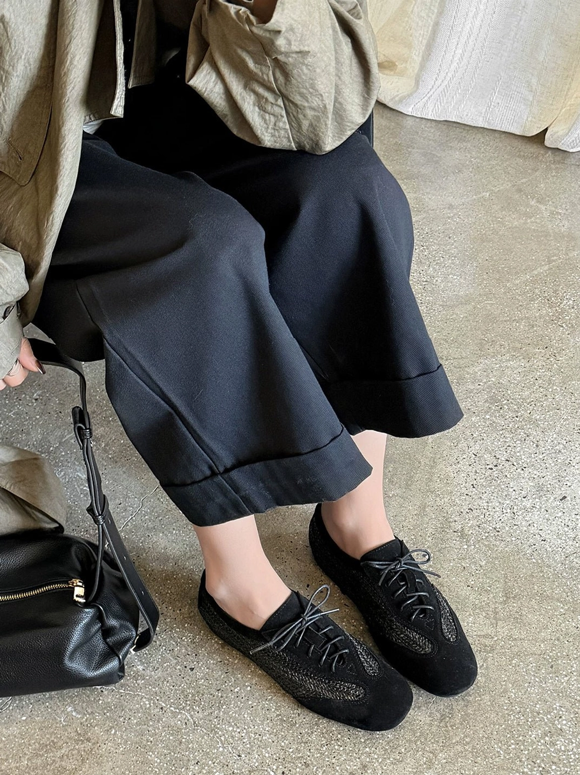All-black woven German trainer sneakers worn with cropped black wide-leg trousers and a black leather shoulder bag for a minimalist streetwear outfit