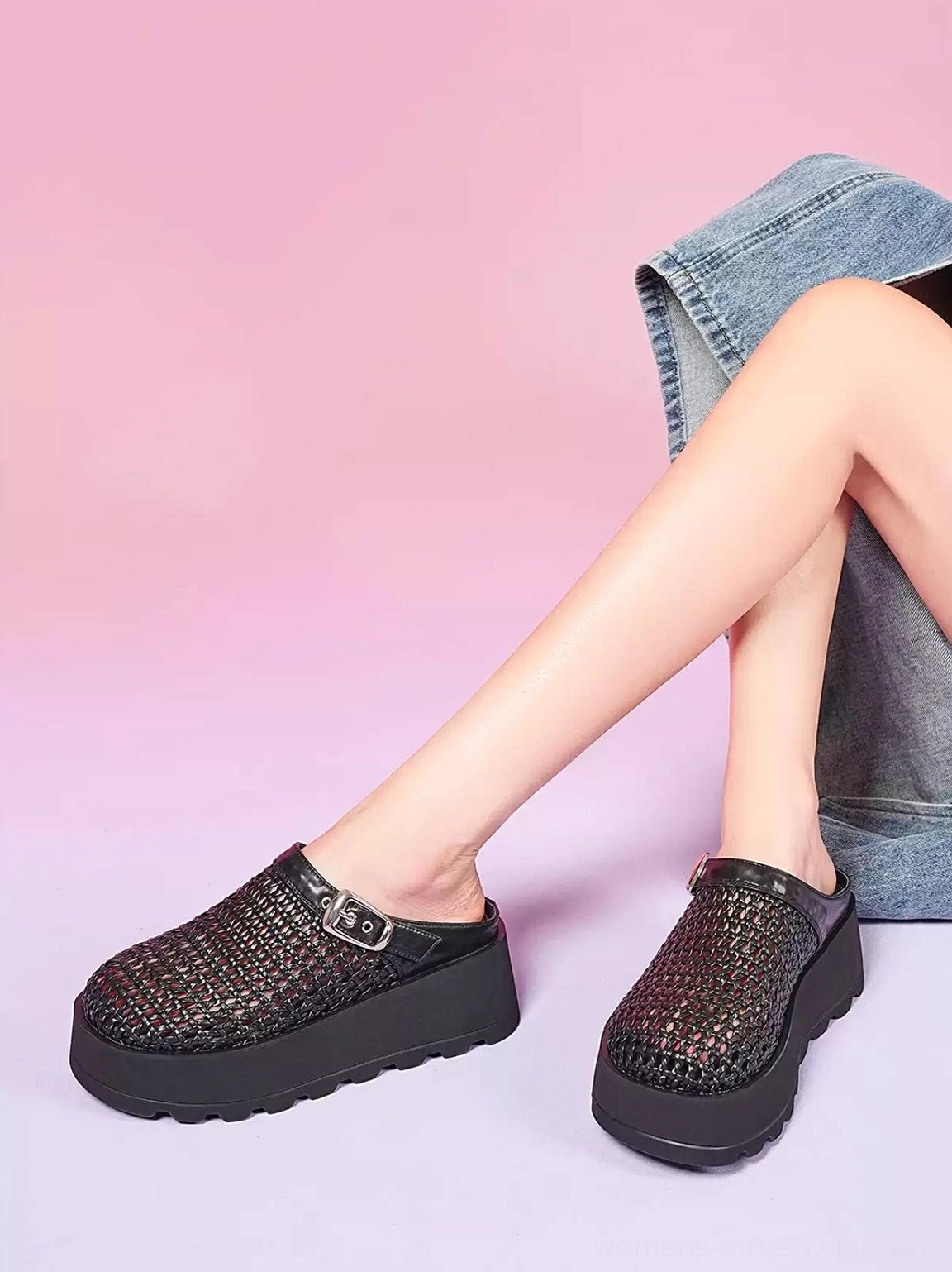 Front view of black woven platform mules worn with denim clothing showing the cutout upper, silver buckle and elevated sole