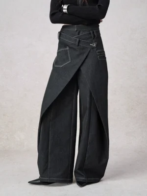 Three-quarter view of black women's wrap front wide leg jeans showing adjustable buckle waistband, layered asymmetric panel, and floor-length streetwear fit
