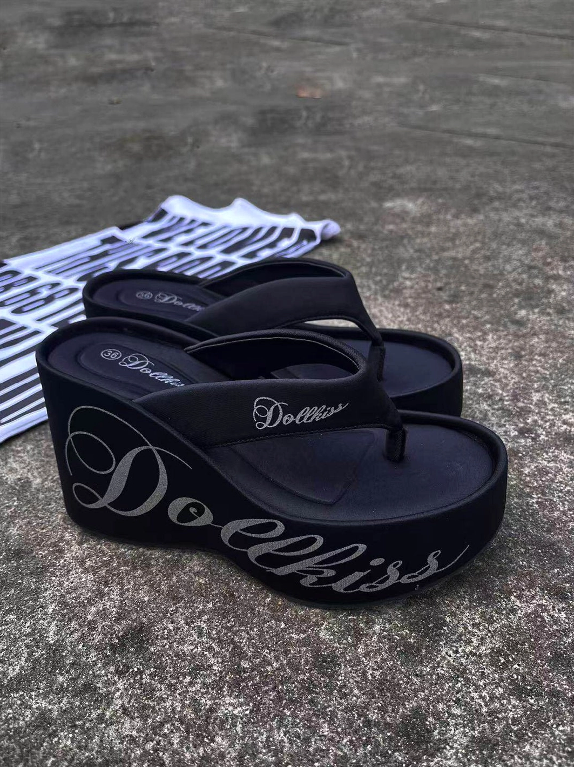Black Y2K logo print 10cm platform wedge flip-flops shown from above on a striped fabric backdrop