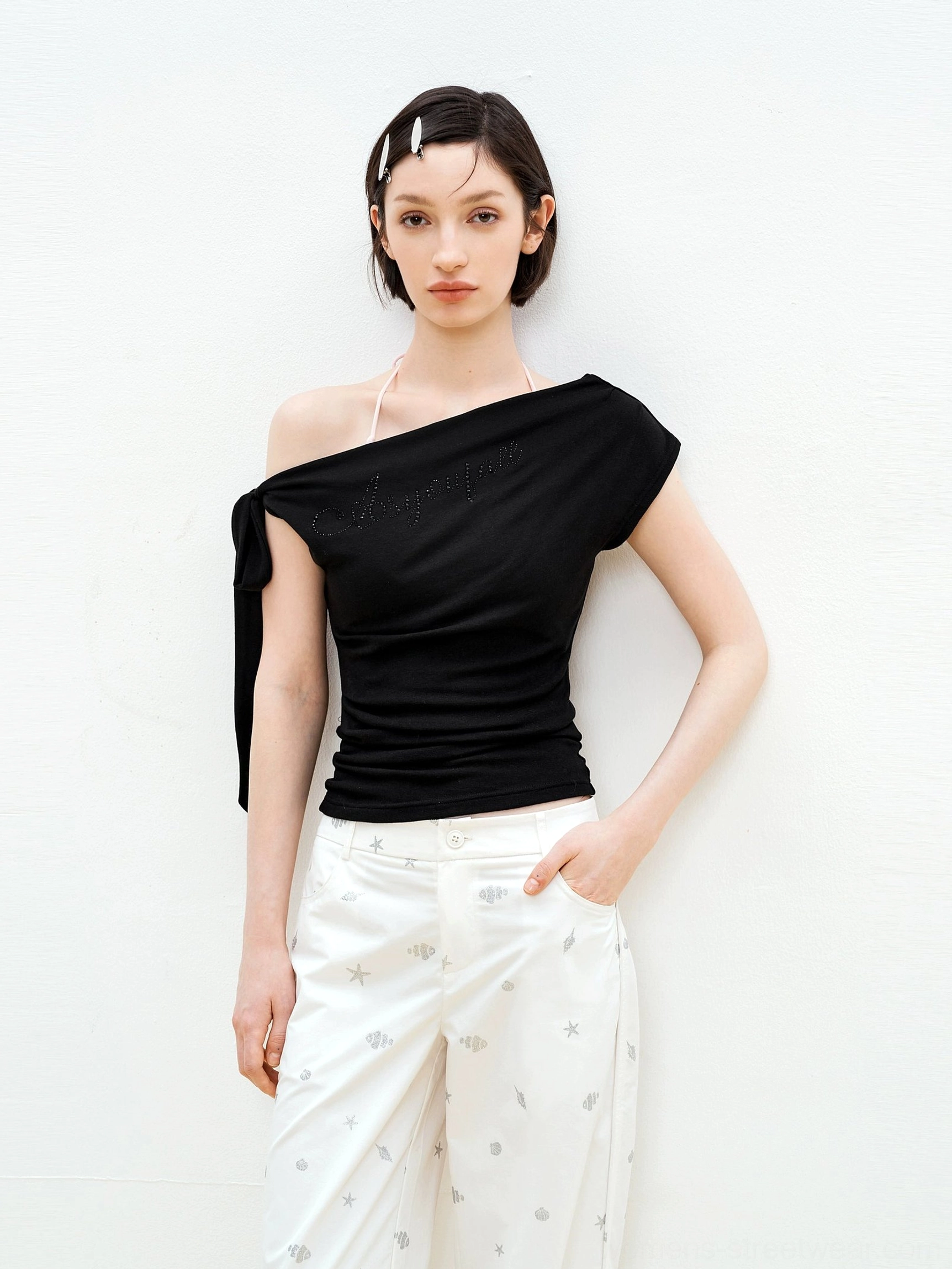 Black Y2K rhinestone asymmetric one-shoulder fitted top styled with white star print wide-leg pants in a studio