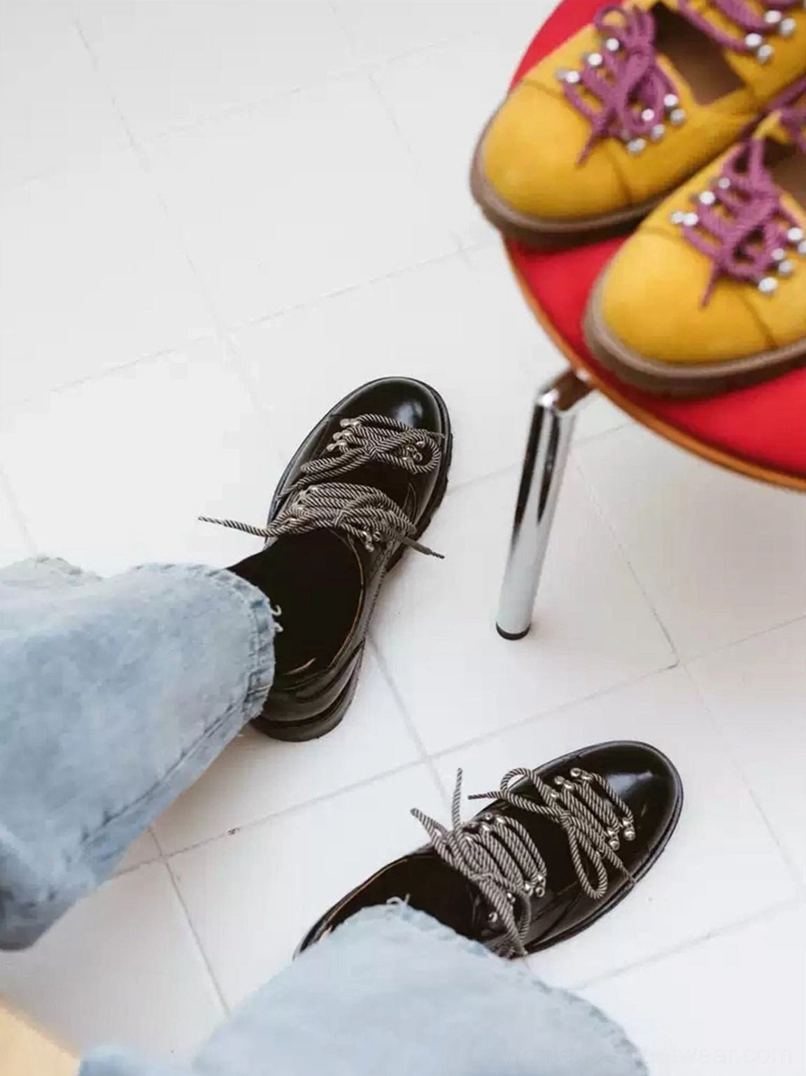 Overhead view of black and mustard yellow chunky workwear derby shoes with contrasting braided laces and rugged lug soles styled with light-wash jeans