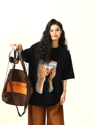 Front view of a black oversized cotton streetwear T-shirt with expressive blindfolded face artwork, brown wide-leg trousers, and tote bag