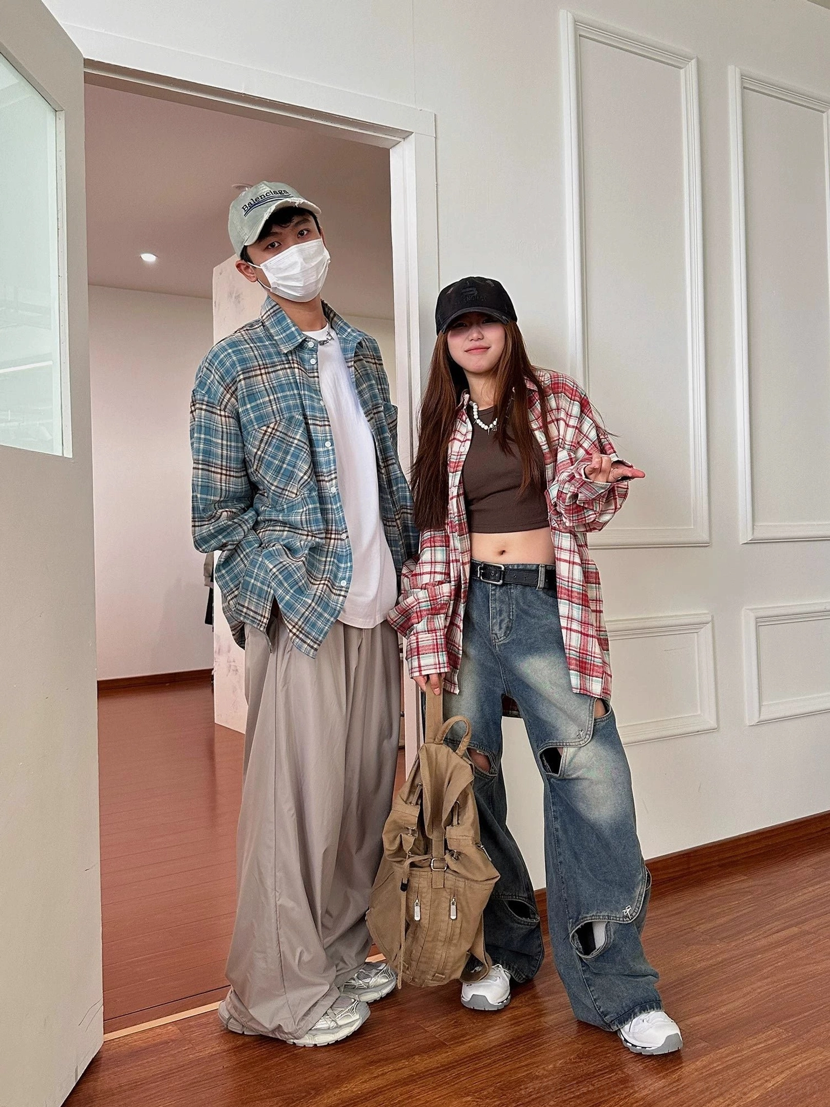 Two models wearing blue brown and red white oversized plaid flannel shirts styled with casual streetwear bottoms