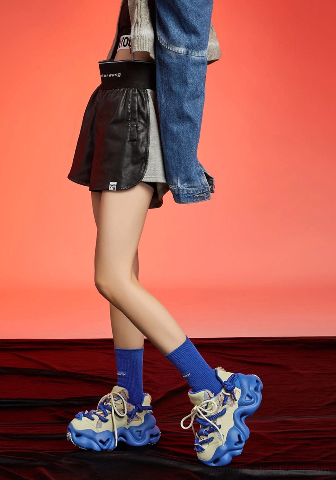 Blue and cream chunky platform sneakers worn with black leather shorts, blue crew socks, and a cropped denim jacket