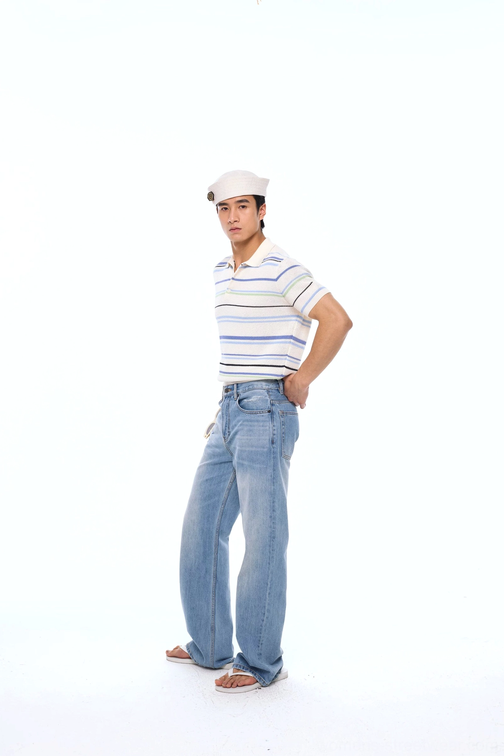 Full-body side-front view of a blue and cream striped openwork knit polo shirt styled with wide-leg light wash jeans and casual summer footwear