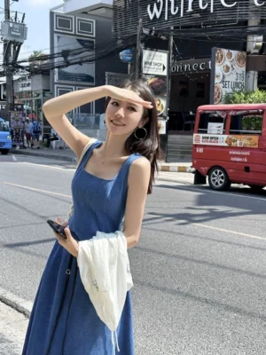 Blue denim square-neck maxi dress with wide straps and fitted waist worn in a modern outdoor street style portrait