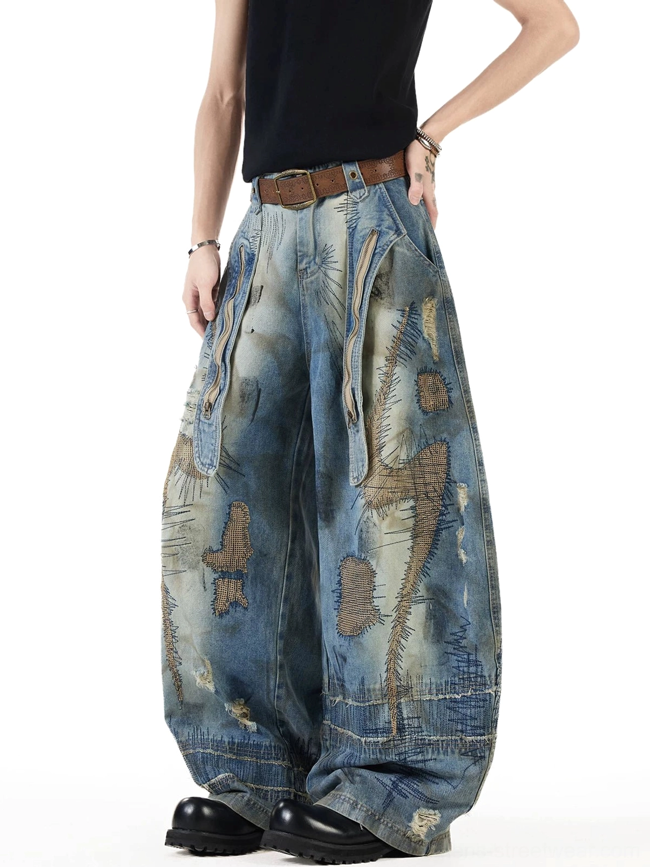 Side three quarter view of blue distressed balloon jeans with intricate patch embroidery, front utility pockets, faded yellow denim accents, and frayed hem details