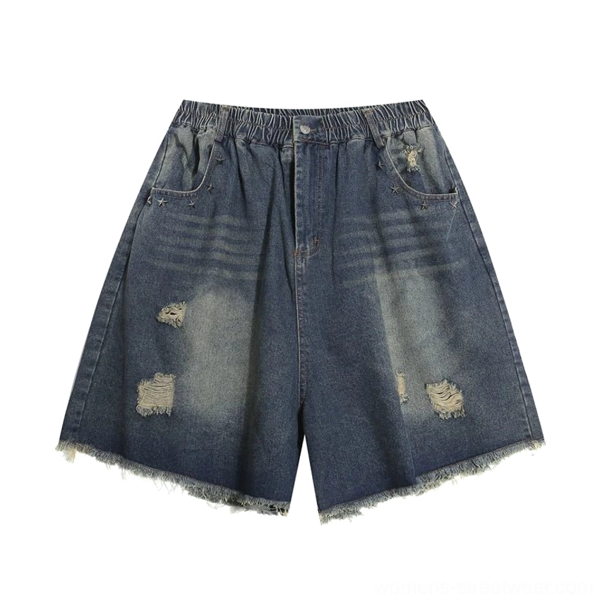 Flat lay of blue distressed denim Bermuda shorts showing elasticated waistband, front slash pockets, ripped accents, wide-leg shape, and frayed hems