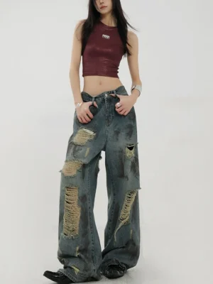 Three-quarter front view of relaxed blue distressed wide-leg jeans with dirty faded wash and shredded leg details