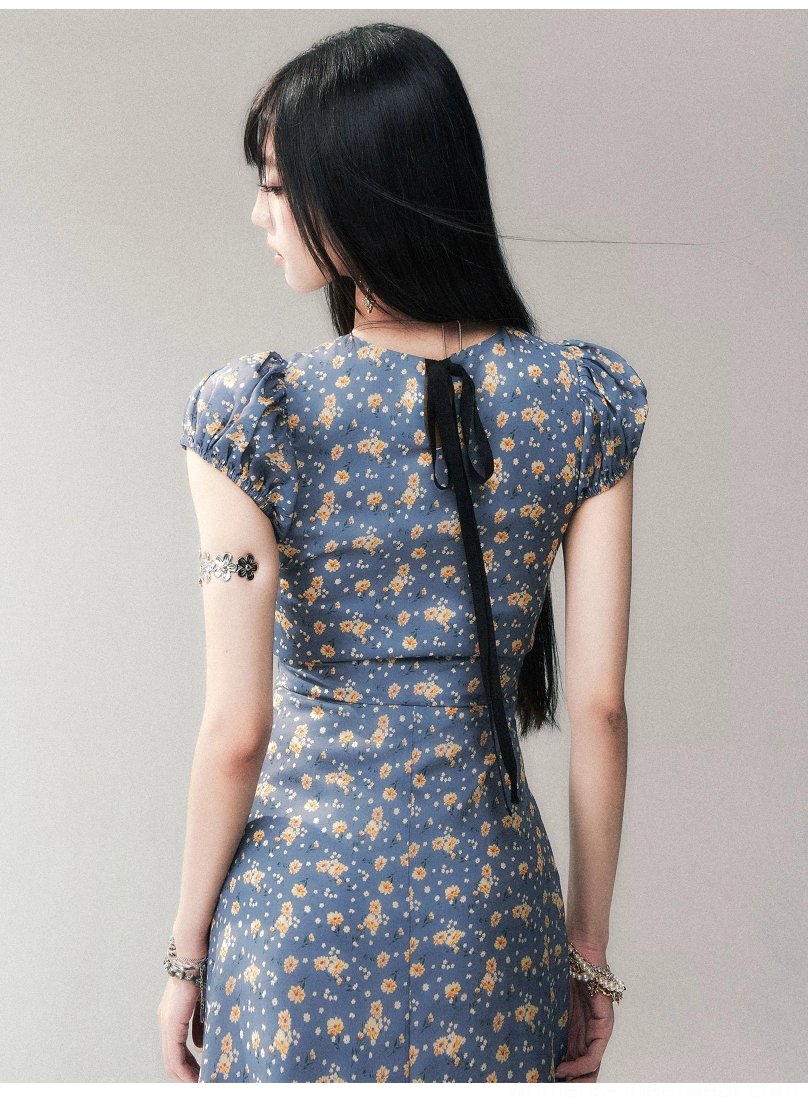 Back view of blue floral open-back maxi dress featuring black ribbon bow detail and puff short sleeves