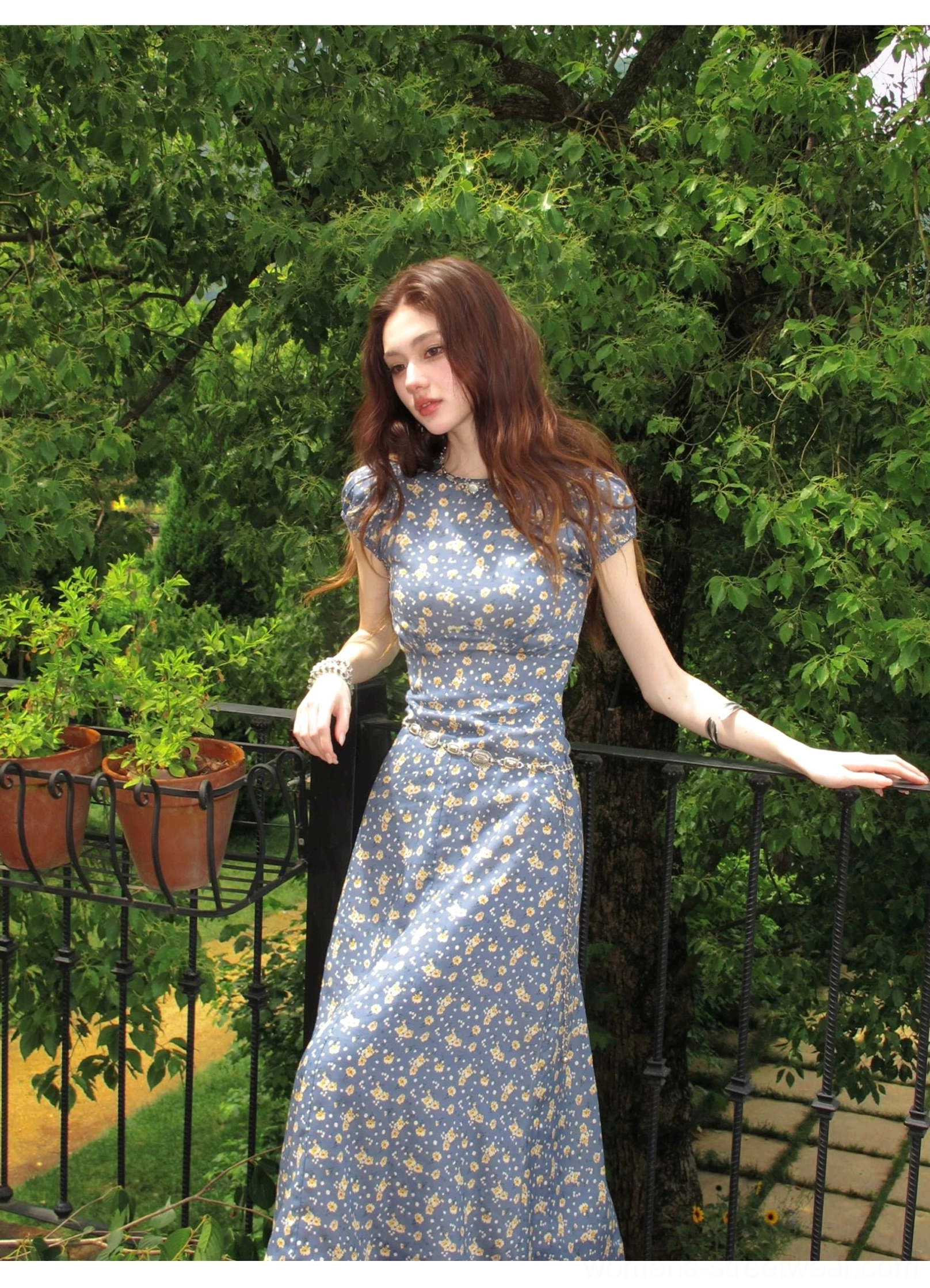 Blue floral puff sleeve maxi dress with round neckline and yellow ditsy flower print in an outdoor garden setting