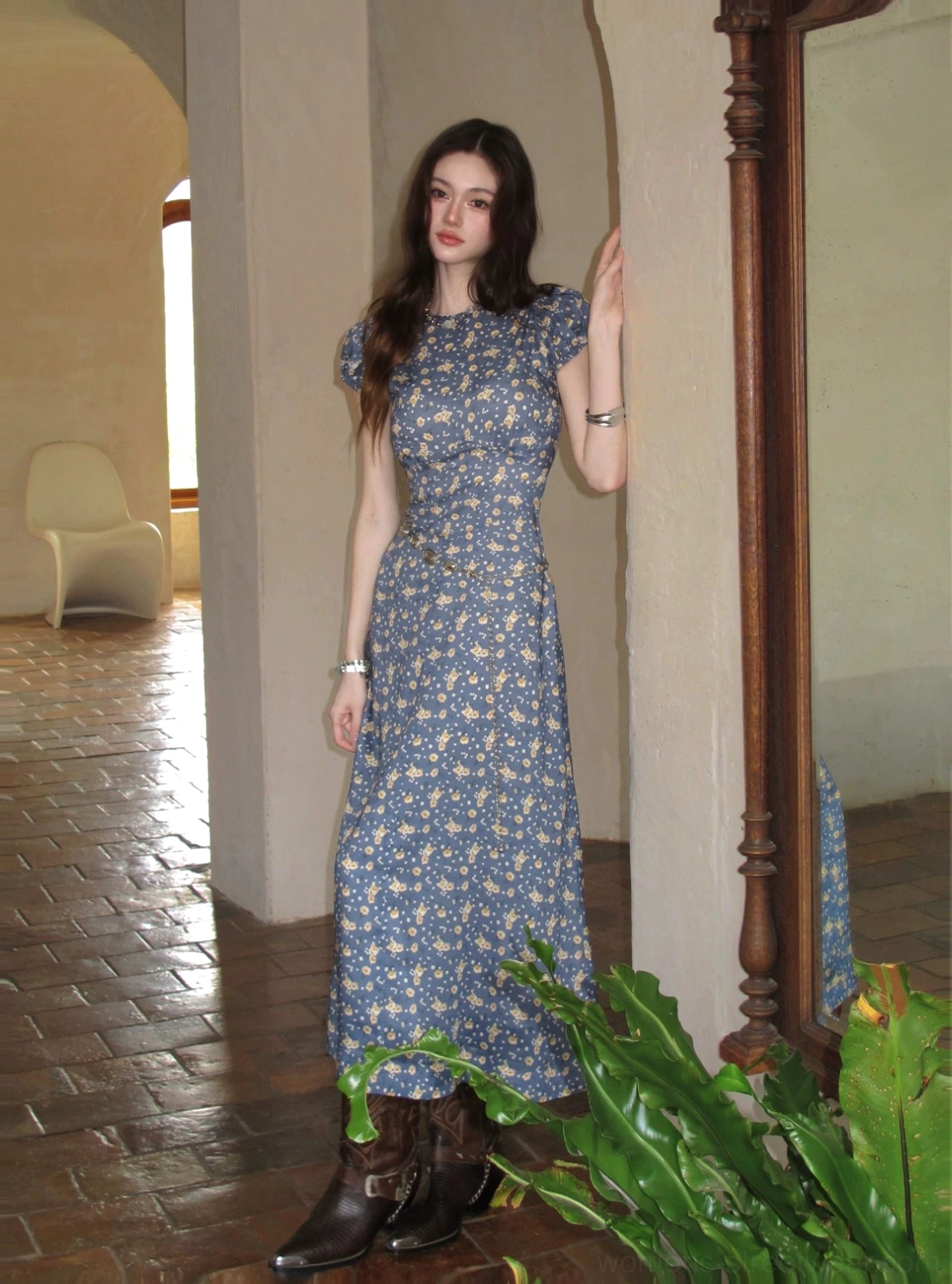 Blue floral open-back maxi dress styled with brown cowboy boots in a vintage tiled corridor side view