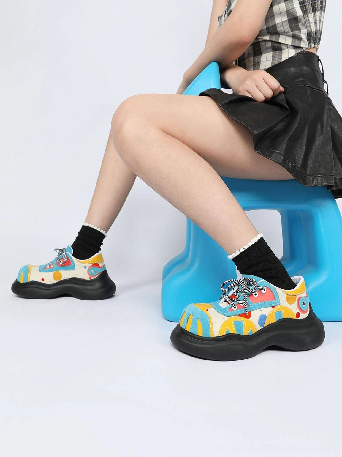 Blue graffiti platform derby shoes side profile styled with black frilled socks, leather skirt, and blue stool
