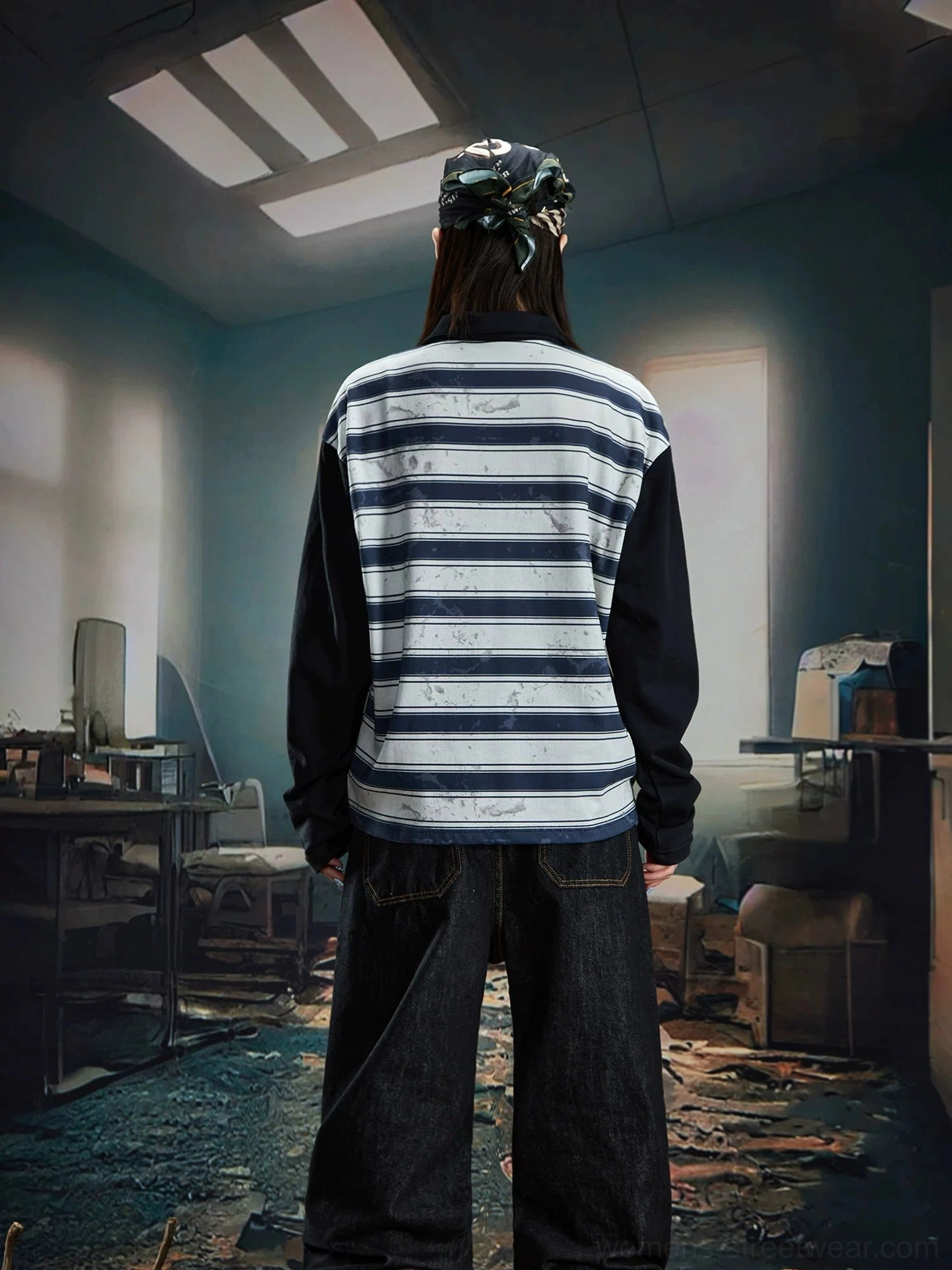 Back view of a female model showing the plain blue grey horizontal striped back of a relaxed rugby polo shirt with dark baggy jeans
