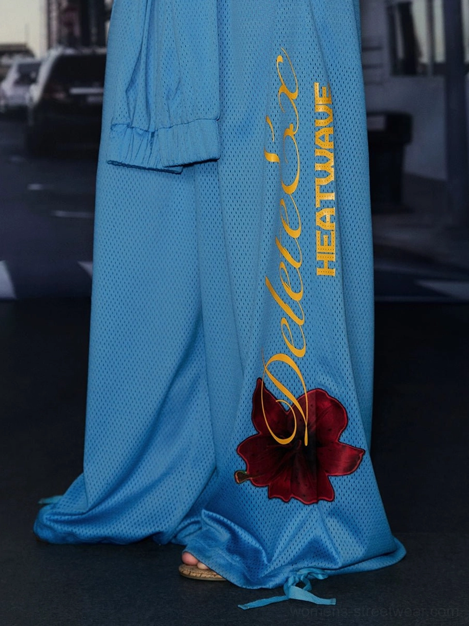 Close-up of blue mesh texture wide-leg streetwear pants with yellow script logo hibiscus detail and drawstring hem