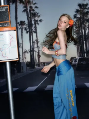 Blue hibiscus wide-leg streetwear pants with tied waist and side script graphic in coastal dusk setting
