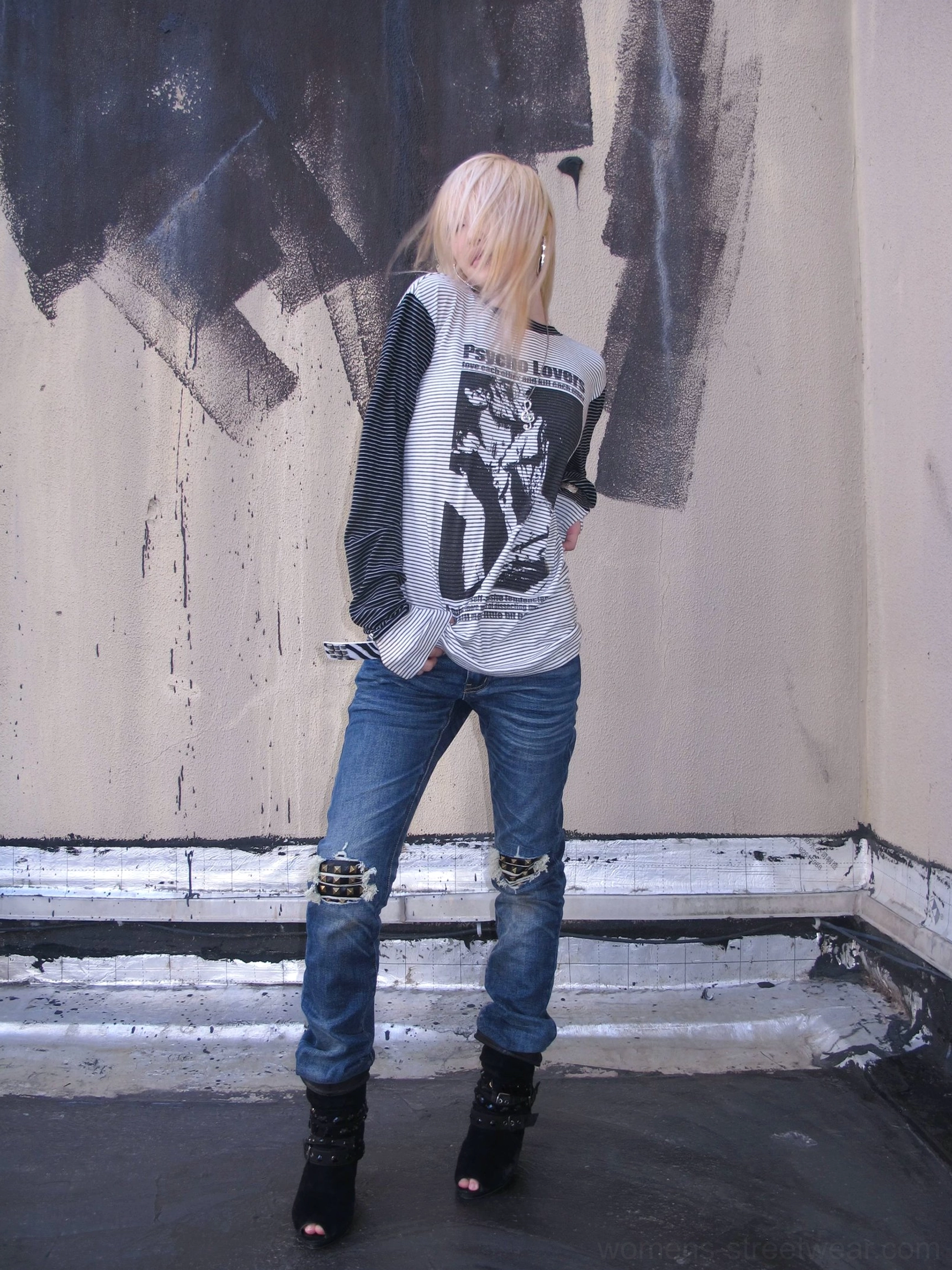 Back three-quarter view of blue knee-distressed slim jeans showing the tapered leg, faded denim wash, and exposed knee patch construction