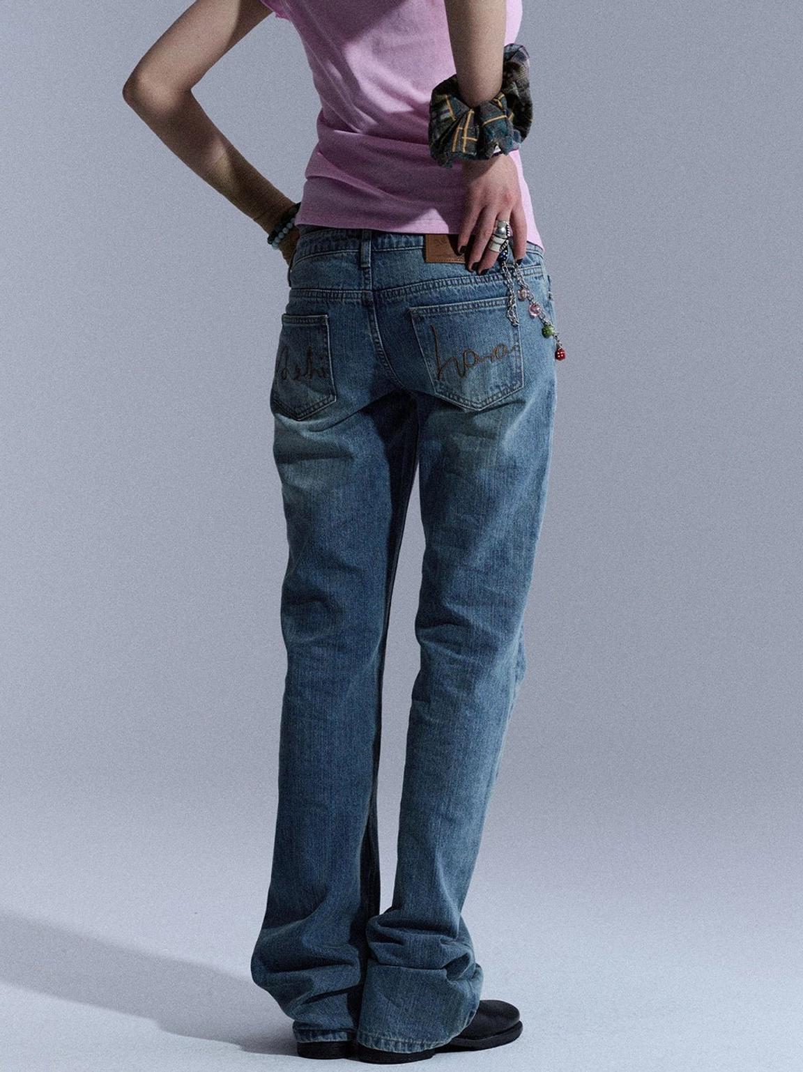 Back partial view of blue vintage wash low-rise flare jeans with decorative waist chain and fabric accents styled for streetwear