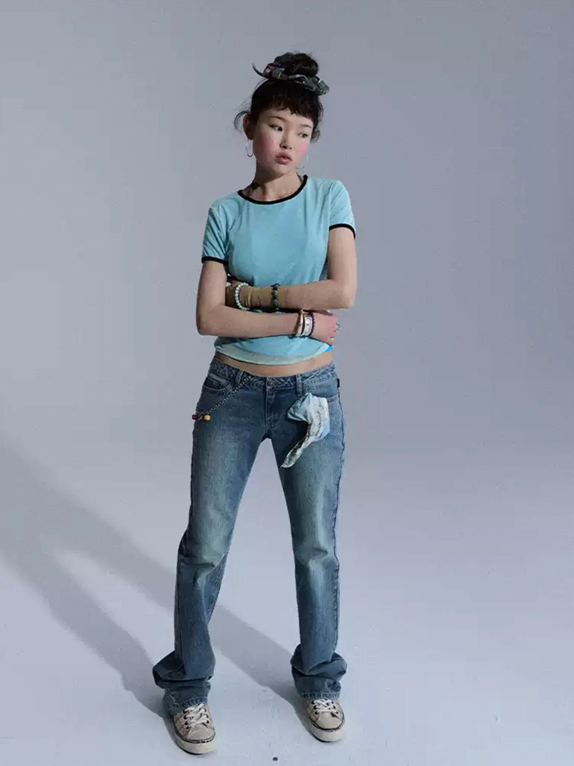 Front streetwear outfit featuring blue low-rise slim flare jeans with printed fabric detail, cropped top, and layered accessories