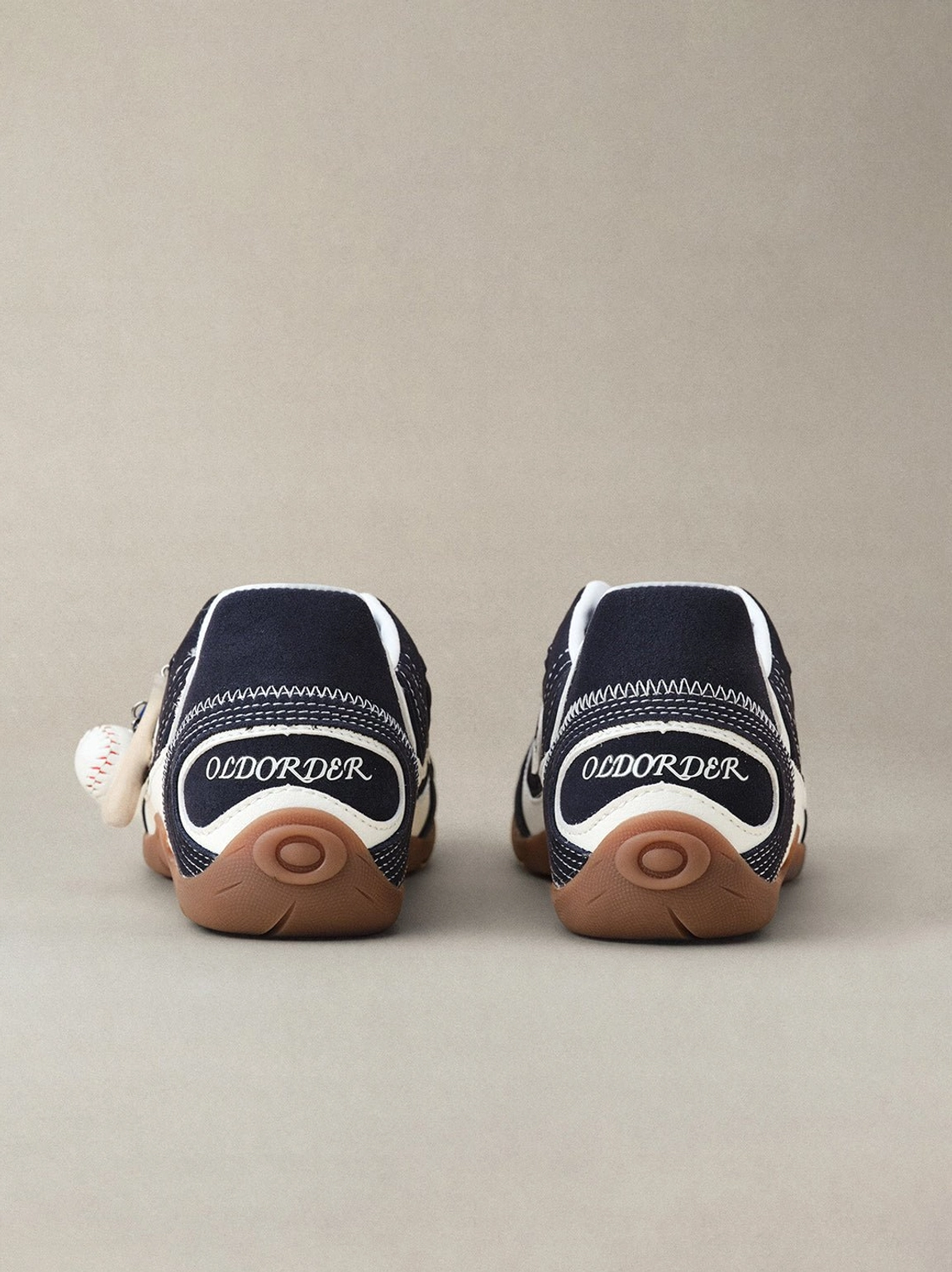 Blue and navy low-profile trainers with contrasting swirl details and playful baseball-inspired sneaker charm