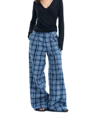Front view of women wearing blue and white plaid high-waisted wide-leg streetwear pants with pleats, a black V-neck top and slide sandals